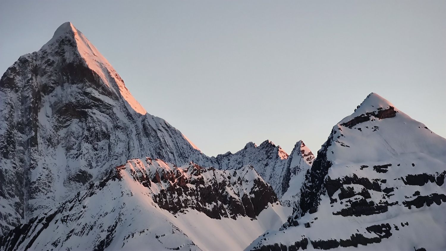 First sunlight turning the summit pyramid of a Siguniang peak pink above the snow ridges at dawn.
