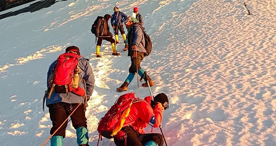Climbers with red backpacks ascend a snowfield in golden early morning light on Siguniang.