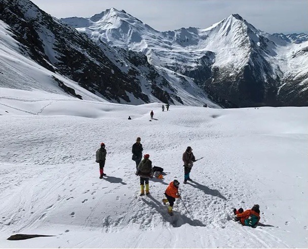 Climbers walking across a wide snowfield below the peaks of Siguniang.