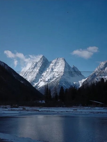 The snow-capped peaks of Siguniang reflected in a calm lake, with dark pine forest in the foreground.