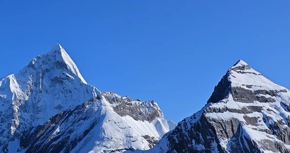 Two sharp snow-covered peaks of the Siguniang massif against a deep blue sky.